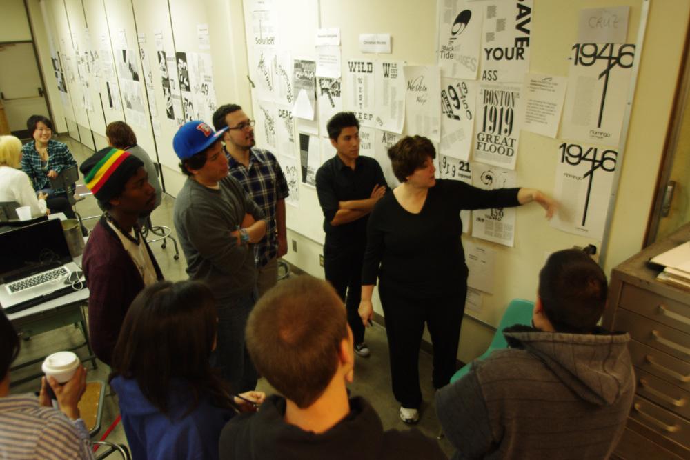 Andrea Micallef, associate professor of art, (left) critiques her student’s latest poster project that required representing an important event in a designated year using only text.  