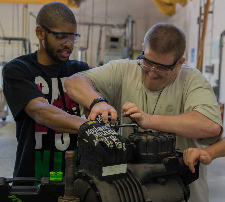 Khris Jackson, 23, Mechanical Engineering (left), and David Witt, 29, Air Conditioning Repair. work together to take apart the reciprocating compressor of an air conditioning unit in order to repair it. The Air Conditioning and Repair department offers students a truly hands-on educational experience. Photo credit: Gilberto Castro
