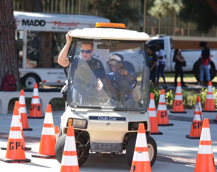 Shadera Woodland, 18, physical therapy major, steers a golf cart while wearing drunk googles as EC Police Officer Matt Ryan holds on while guiding Woodland at the 2014 DUI awareness. ECPD will be hosting the 15th annual DUI awarrness fair on Thursday Oct. 29 near the Library Lawn. Photo credit: John Fordiani