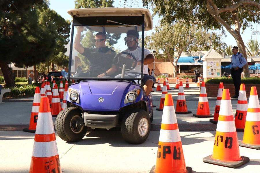 Joseph Taliauli, 19 kinesiology major puts on beer goggles, which simulates being drunk at the legal limit of .08. He then tries to navigate through a course of cones with ECPD officer Matt Ryan during the 15th Annual South Bay DUI Awareness Fair on Thursday. 
Photo credit: Jackie Ramano 