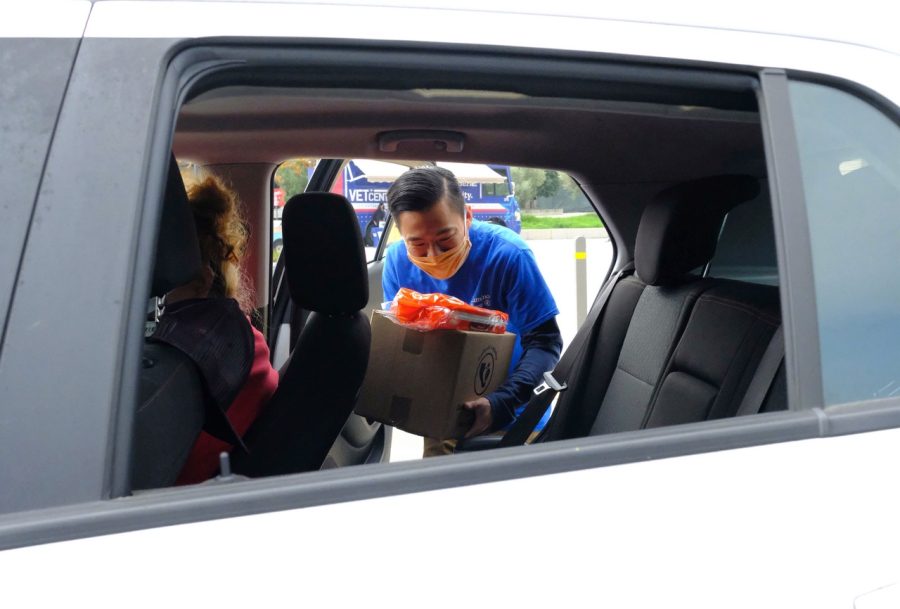 El Camino student success coach, David Ruiz, 27, loads a box of free food giveaways into a car driven by a member of the community during the Veterans and Community Thanksgiving event at ECC. Photo by Jose Tobar/The Union