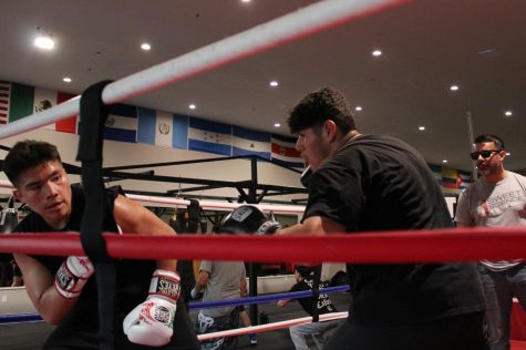 Andy Bocanegra, 15, (L) of Compton, Calif. dodges a punch from David Lopez, 15, of Hawthorne, Calif. at Sweet Science Boxing & MMA Gym in Hawthorne on Thursday, April 7, 2022 while David’s coach, Albert Ugarte (R) looks on. “I hope to become the best by training a lot and sacrificing to get better,” David says. On May 22, the gym is hosted a tournament that several boxers here hoped would be their first opportunity to compete. (Kim McGill | Warrior Life)