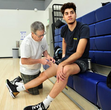 El Camino College men&squot;s volleyball Head Coach Richard "Dick" Blount wraps the right thigh of outside hitter Dylan Garcia at practice March 17, 2022, in the new campus gym. Dylan said he had strained a quadriceps muscle. (Gary Kohatsu | Warrior Life)