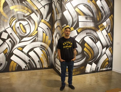 Artist Zak Prez stands in front of his mural, which is a part of the new 'Aqui y Alla y Mas' art exhibit, the exhibit held its public reception on Saturday, Oct. 15 in the El camino College Art Gallery. Perez says he has been experimenting with the recurring theme of subliminal messages, the word 'love' is hidden on his mural. (Delfino Camacho | The Union)