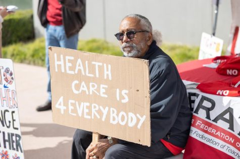 Psychology Professor Michael Wynne holds up a sign requesting better healthcare benefits outside of the Administration Building on March 20. Wynne said whenever the El Camino College Federation of Teachers challenges the opinions of the Board of Trustees, give "very vague" responses. (Khoury Williams | The Union)