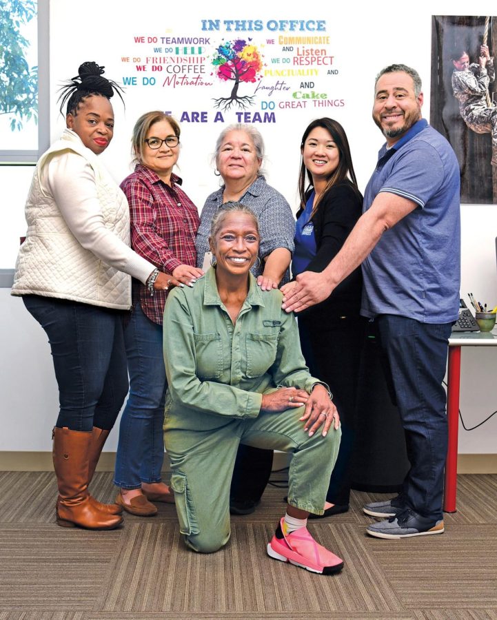 Major Brenda Threatt, kneeling and clad in an Air Force jumpsuit for comfort, is joined by her ECC Veterans Services staff under the office credo. Standing from left are Regina Cook, administrative specialist; Rosanna Merrill, certifying official; Nina Bailey, certifying official; Pryscilla Truong, veteran counselor; and Roland Tony Zapata, veteran counselor. Threatt and her crew service El Camino College veterans with a variety of services and working tools. (Gary Kohatsu | Warrior Life)
