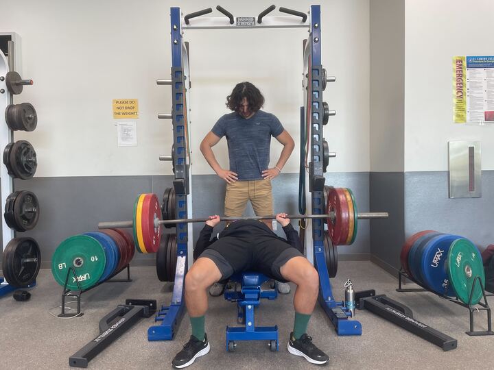 Thanos Barreas, the co-founder, spots the ICC representative, Ace Reyes, as he bench presses in the Pool Classroom Building on Wednesday, Oct. 25. (Joshua Flores | The Union)
