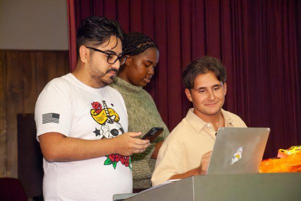 Vice President Kenjy Bervera, Event Planner Victoria Crudup, and President Aiden Ross stand at the podium preparing a kahoot session during the first meeting of the Scene One film club.