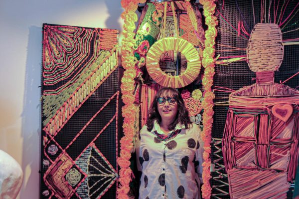 Coordinator of the Dia De Los Muertos exhibit, Dulce Stein, stands inside a woven casket donated by UCLA art students who made it. The piece carries a lot of symbolism as the golden halo above creates a heavenly glow that is supposed to represent the overlooked beauty death can hold. (Isabelle Ibarra| The Union)