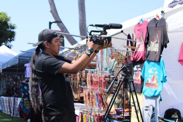 El Camino College film major Tyler Notah films merchandise at a vendor booth at the 11th Annual Native American Indian Pow Wow at California State University, Dominguez Hills in Carson, Calif., on Sunday, April 21. Notah is a content creator with over 44,000 followers on his TikTok channel @native.hustle. (Elsa Rosales | Warrior Life)