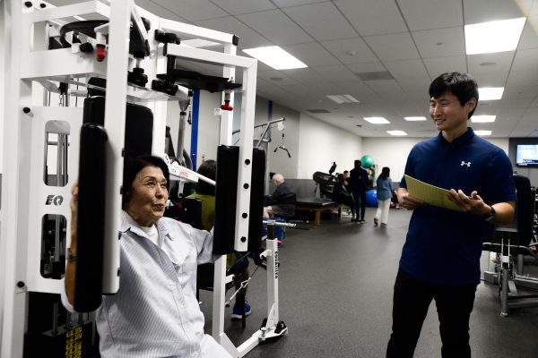 Carole Hoshiko does chest exercises on a multifunctional weightlifting station on Oct. 24, 2024 at the Adapted Fitness Room as Adapted Physical Education Coordinator Jae Lim looks on. (Angel Pasillas | Warrior Life)