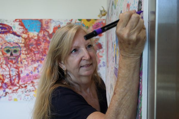 Carrie Lockwood, El Camino College Art Gallery associate, points a purple marker in front of the doodle art wall inside the gallery on Thursday, Oct. 10. Lockwood, 62, is an associate at the gallery where she helps manage, plan and organize artwork that goes into the gallery for exhibitions.