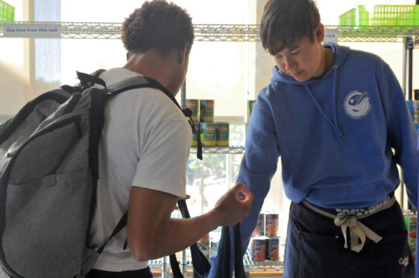 Bryan Lankin, 23, an employee working at the Warrior Pantry, aids in putting essential canned items in a student's shopping bag on Tuesday, Nov. 12, 2024. The Warrior Pantry offers an extensive range of fresh and canned foods. (Argentina Talley | The Union)