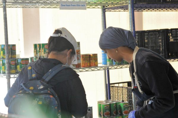 Tesnim Shami, 18, an employee at the Warrior Pantry, assists a student in selecting from the many various canned foods provided there. (Argentina Talley | The Union)