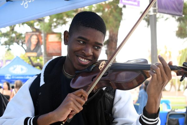 Music and biology major Conner Bailey, 21, tries playing the violin for the first time at the El Camino College Society of Music’s table at Club Rush on Wednesday, Sept. 10. Bailey is learning to play the piano but has the most practice with the saxophone. “[The violin] is like nothing I’ve ever held before. It’s very unique and I can see why it’s the hardest [to play],” Bailey said. (Nikki Yunker | The Union)