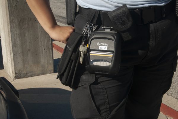 Cadet Hurtado wears a Zebra mobile printer, this printer is what the El Camino College police team use to issue parking citations across campus. According to Hurtado, the campus police focus on vehciles who are either illegally parked or parked in designated staff parking spaces. (Isaac Ramirez|The Union)