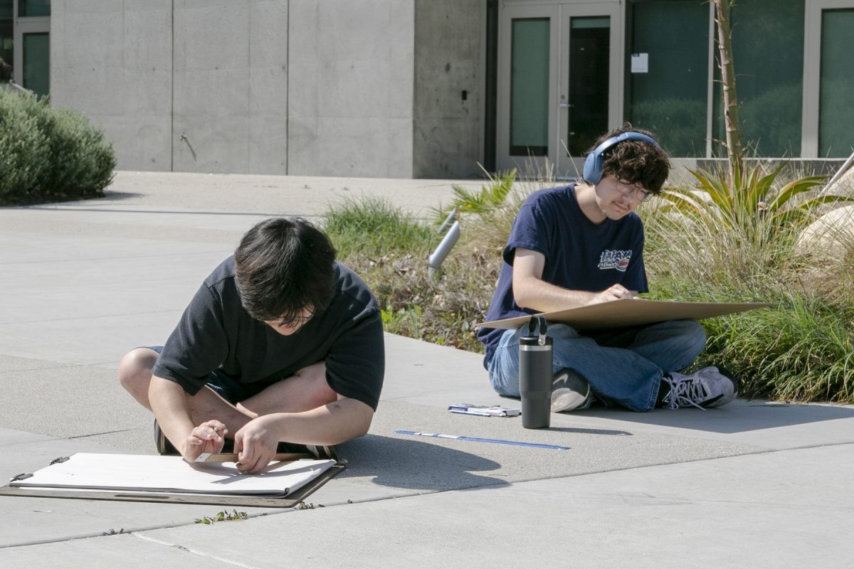 (L to R) Eugene Choi, 19, and Gavin Walz, 19, both art major, draw outside of the Arts Complex building on Tuesday, March 24. Walz said he thinks AI art is soulless. (Frances Que | The Union)